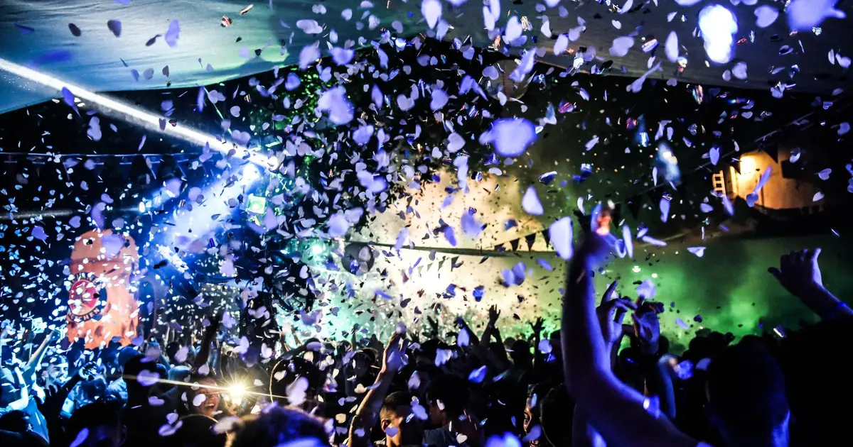 Feiernde Gäste im Club unter Konfettiregen und blauem Licht, Hände in der Luft