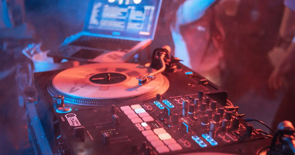 DJ-Pult mit Plattenspieler, Mixer und Laptop in rot-blauem Clublicht – Ticketing für Clubs und Partys